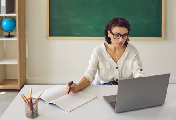 istock School teacher sitting at desk with laptop and having online class with students 2193150931