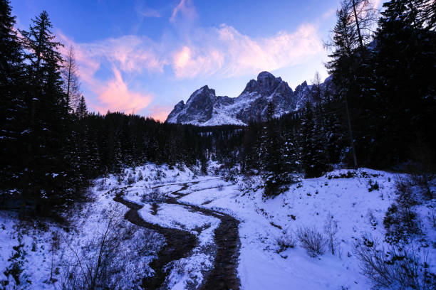 Moody sky over mountains and stream in winter at sunrise, Dolomites