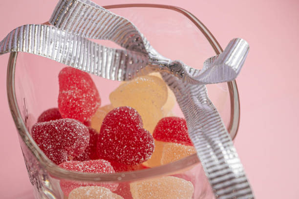 Gummy hearts in a glass with silver ribbon on a pink background