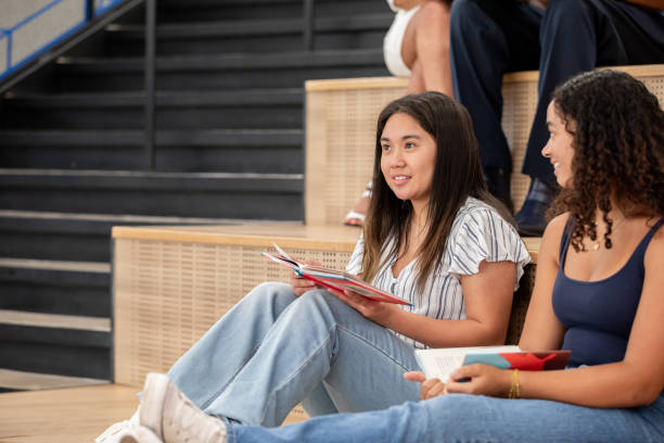 istock Two teenagers discuss a book they are reading together while perched on the library stairs. 2193158306