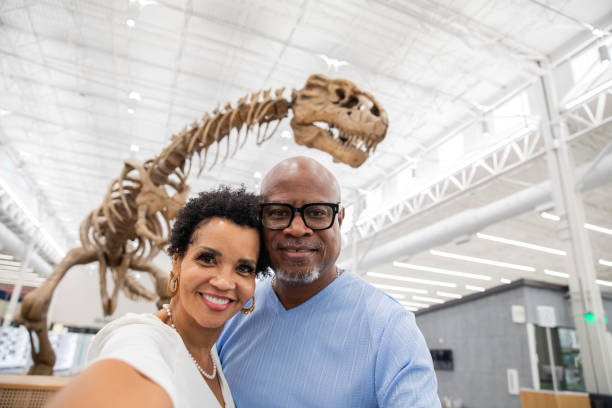 istock A retired couple snaps a selfie with a T-rex fossil displayed in the background. 2193158329