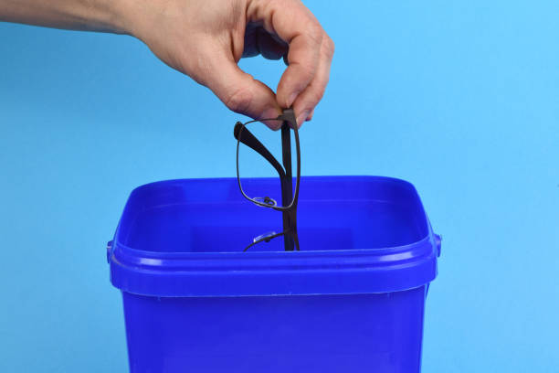 istock Hand holding plastic black glasses puts in blue container, isolated on white background. 2193158500