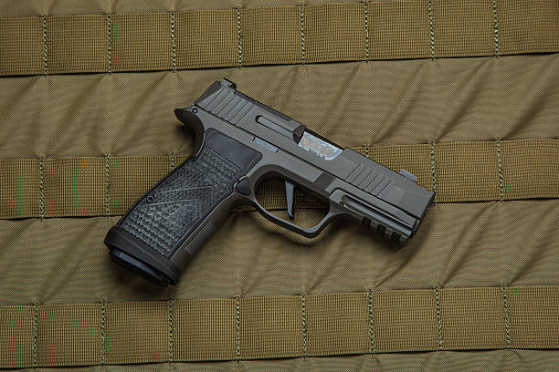 A black handgun with a textured grip placed on a green tactical fabric background, showcasing its design and details, ideal for law enforcement, military, and self-defense themes.