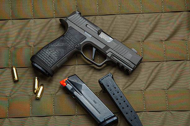 istock A black handgun with a textured grip, two magazines, and four bullets displayed on a green tactical fabric background, emphasizing the firearm's features and accessories. 2193158693