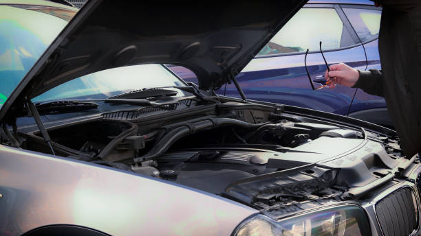 Mechanic holding glasses, inspecting a car engine with the hood open
