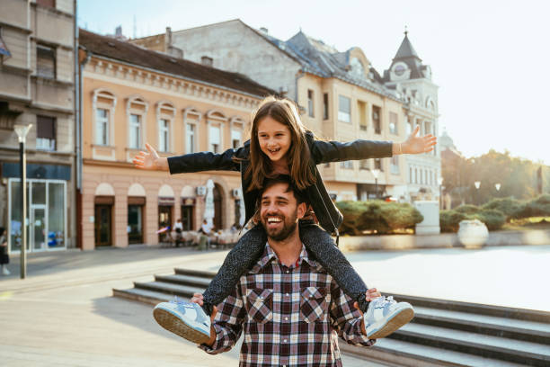 istock Father carrying his daughter on shoulders, both smiling joyfully in bright urban setting during golden hour, while enjoying travel and city break 2193168709