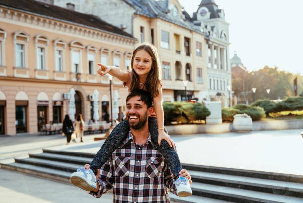 istock Father carrying his daughter on shoulders, both smiling joyfully in bright urban setting during golden hour, while enjoying travel and city break 2193168728