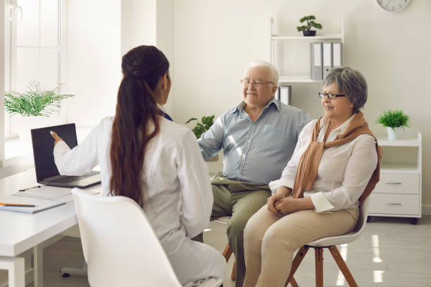 Happy mature couple and their doctor communicating while using laptop during medical appointment.