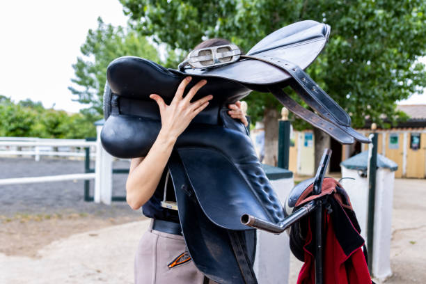 istock Equestrian woman carrying saddle in riding stables: preparation and care 2193172191