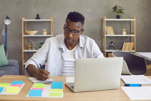 istock Young african american man sitting at desk working on laptop computer from home 2193173831