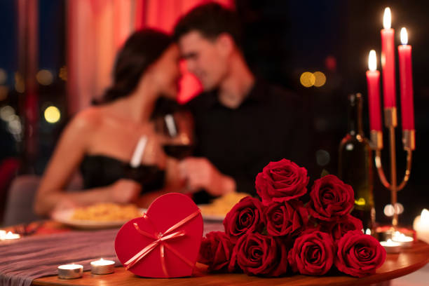 istock Romantic Valentine's dinner. Couple in love cuddling on background, having date in atmospheric restaurant interior in the evening. Selective focus on flowers and gift box 2193175925