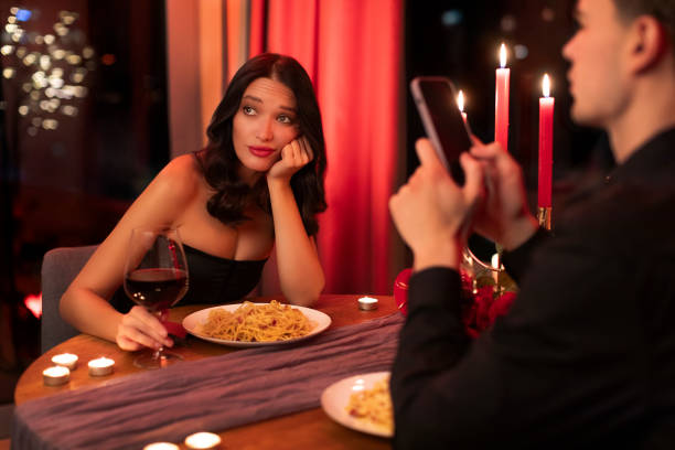istock Boring date. Man using smartphone in restaurant and ignoring his girlfriend during romantic dinner, sitting at table 2193176678