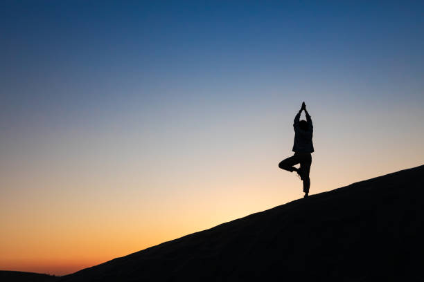 istock Silhouette of a woman practicing yoga in a balanced pose on a sand dune at sunset. Capturing mindfulness, serenity, and harmony in a peaceful outdoor setting under a colorful evening sky. 2193182962