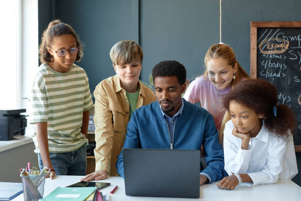istock Male Teacher with Group of Kids Using Computer in Class Smiling 2193187515