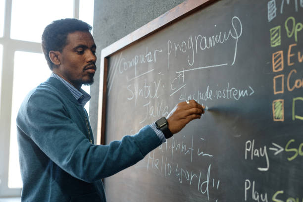 istock Black Male Teacher Writing on Blackboard in IT Class 2193187524
