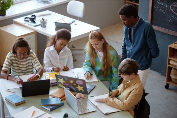istock Group of Kids Working at Big Table in Class with Male Teacher Watching 2193187565