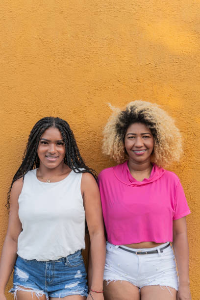 istock Two smiling women posing against yellow wall 2193190956