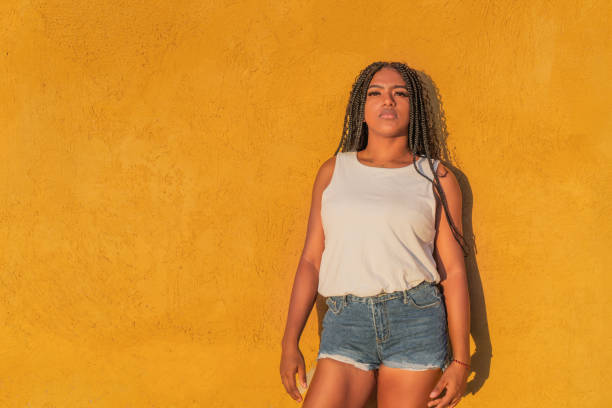 istock Young woman with braids posing against a vibrant yellow wall 2193191533