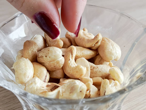A woman's hand takes a cashew nut from a cup. A plate of cashews is on the table. A healthy snack. Calorie content of nuts.
