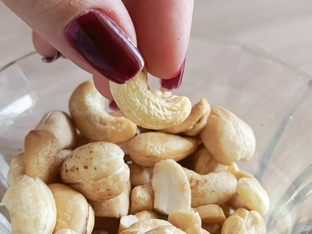 A woman's hand takes a cashew nut from a cup. A plate of cashews is on the table. A healthy snack. Calorie content of nuts.
