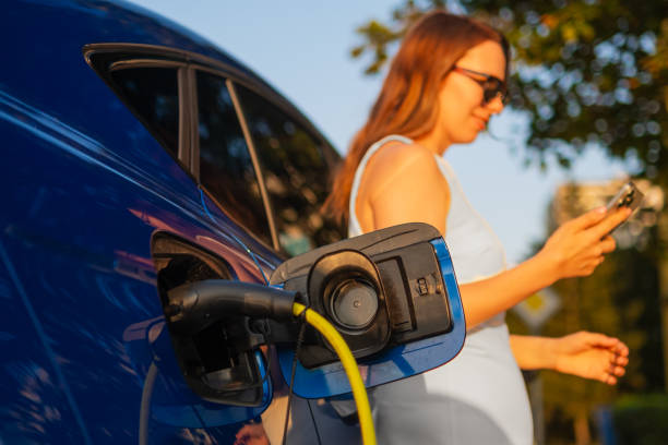 istock Woman in white dress using smartphone while charging electric vehicle in sunlight. 2193199700