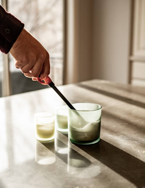 istock A close-up of a hand using a lighter to light candles in glass jars on a reflective surface, with soft natural light and shadow 2193202049