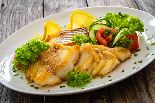istock Fried codfish loin and fresh vegetables served on white plate on wooden table. 2193209747