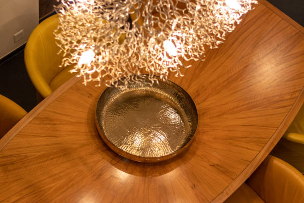 istock A wooden dining table with a golden decorative plate, surrounded by yellow chairs, and a chandelier overhead 2193216681