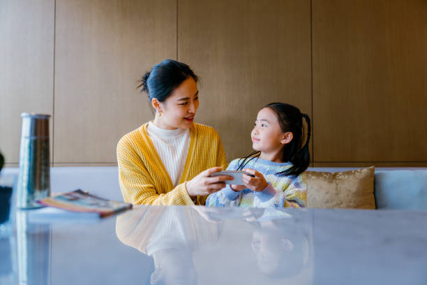 Young Asian mother and lovely little daughter studying together on digital tablet while a break from mom's business trip. Working mom managing work life and childcare at business trip.