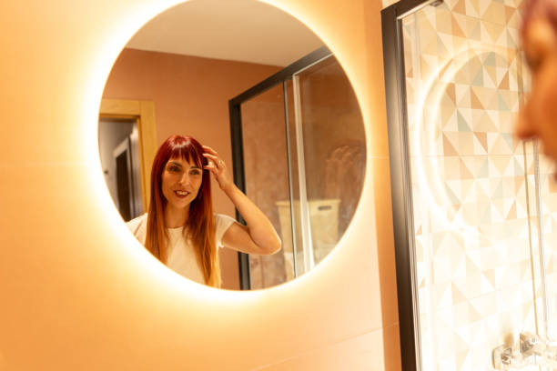 istock Beautiful woman adjusting hair while looking at herself in bathroom mirror 2193223509