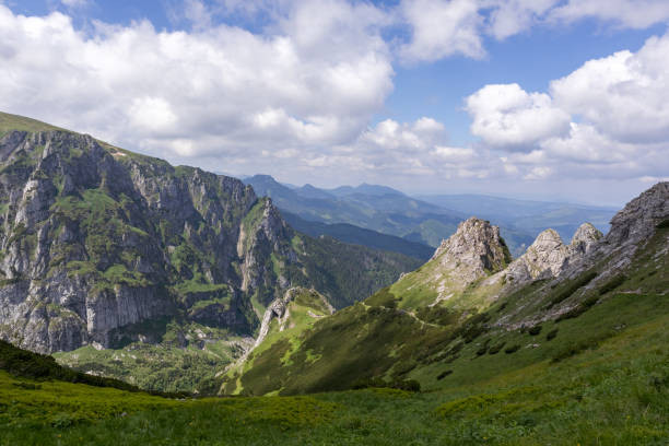 istock .A mountainous area with jagged peaks partially covered with snow and green slopes, white clouds can be seen in the sky. 2193223571