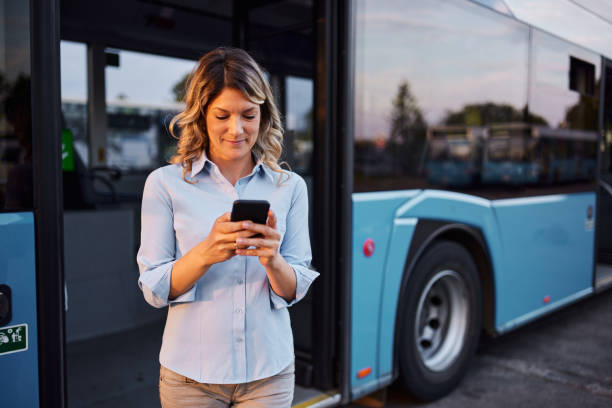 istock Smiling woman using cell phone by the bus at station. 2193226504