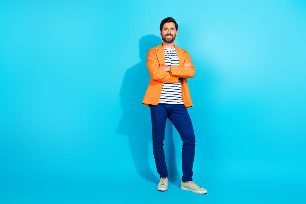 istock Confident man in bright orange jacket standing with crossed arms against teal background, showcasing style and charisma. 2193226830