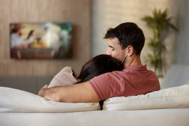 istock Back view of embraced couple watching TV on sofa at home. 2193227050