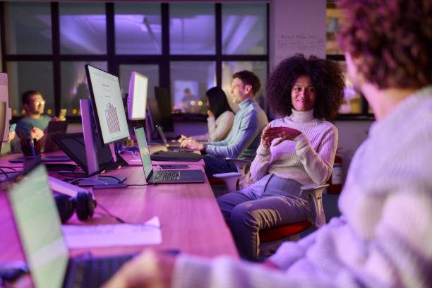 Smiling black programmer talking to her colleague late in the office.