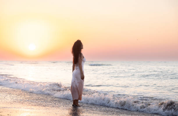 Romantic and fairytale view of a wonderful sunrise at seaside and a young woman admiring and enjoying the moment.