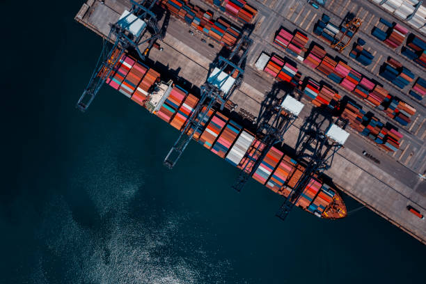 istock commercial port in deep sea load and unloading cargo from container ship import export by crane for distributing goods by trailers transport logistic  to customers and dealers, aerial top view 2193237429