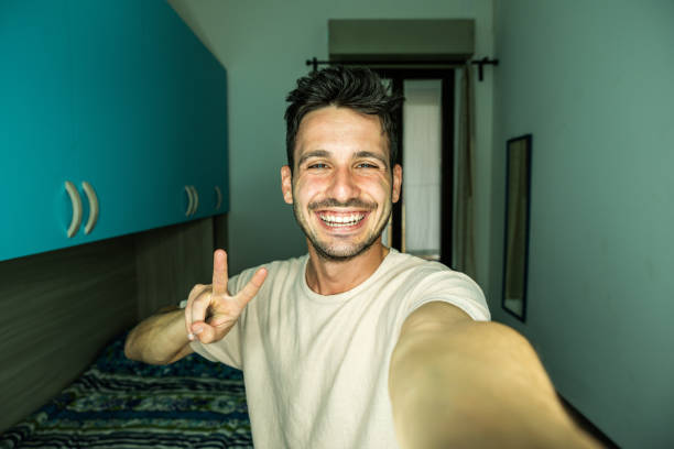 Happy handsome guy taking selfie with smartphone at home - Laughing guy looking at camera - People and technology concept