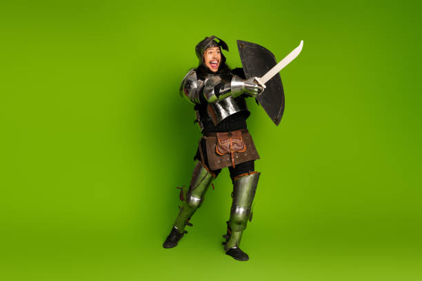 istock Medieval knight in armor holding sword and shield on bright green background 2193243157