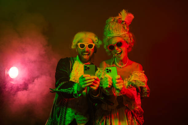 istock Elegant noble couple in vibrant costumes using smartphones under dramatic lighting at a themed party 2193243804