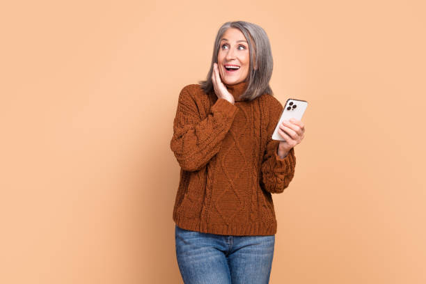 istock Charming Elderly Woman Expressing Joy While Holding Smartphone Against a Beige Background 2193247041