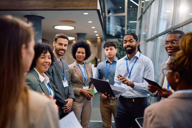 istock Black entrepreneur using laptop while talking to group of business seminar attendees in a hallway. 2193248165