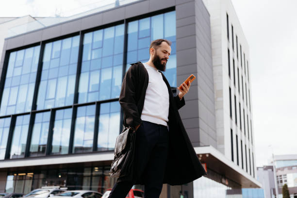 istock Businessman walking and using smartphone in front of modern office building 2193248389