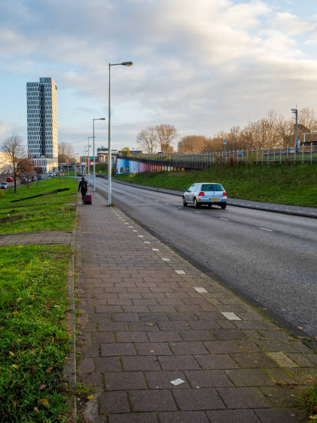 Amsterdam, Netherlands - Nov 29, 2019: Suburban road with vehicle and pedestrian traffic. Modern buildings around the area.
