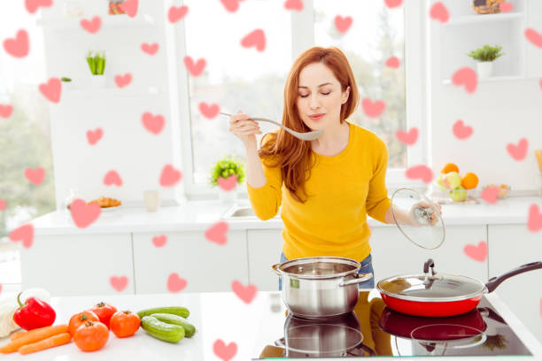 istock Lady in yellow pullover, with tomato, cucumber, pepper, cabbage, carrots on the table in modern white bright cozy, comfort interior make yummy dish for breakfast for family 2193260939