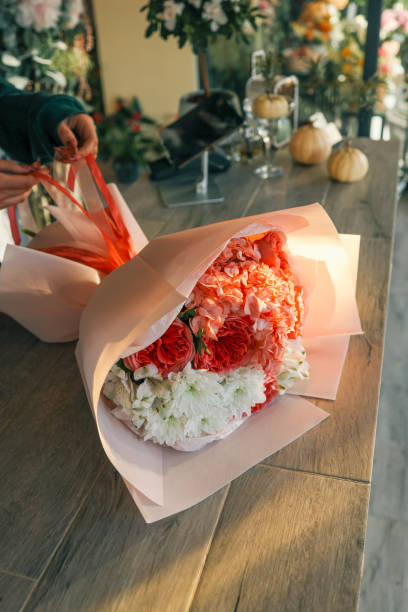 istock Close-up of a luxurious bouquet featuring vibrant red roses, delicate hydrangeas, and white alstroemerias, elegantly arranged and wrapped in soft pastel paper on a wooden counter 2193264626