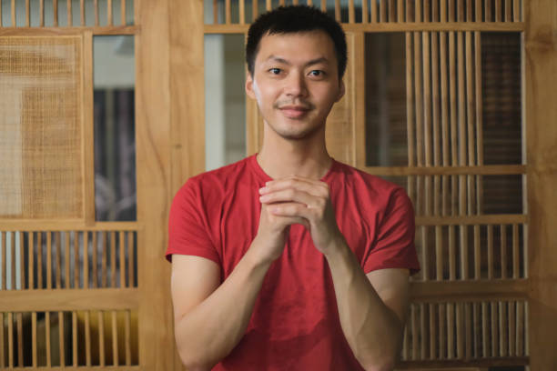 Shot of Chinese Man With Gongxi Hand Gesture on Chinese New Year. Concept: Chinese culture, Gongxi gesture, New Year celebration, traditional greeting, cultural heritage, festive attire, Lunar New Year, Chinese traditions, joyful moment, prosperity wishes, holiday spirit, heritage appreciation, cultural expression, symbolic gesture, seasonal festivity.