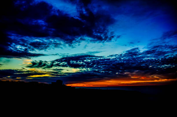 A beautiful blue sky with a few clouds and a sunset. The sky is very dark and the sun is setting