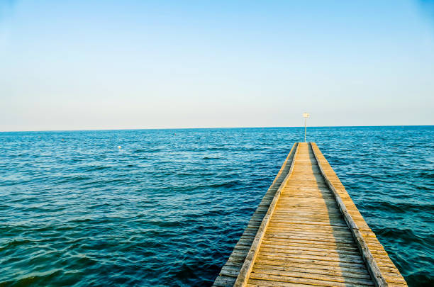 A pier is shown with a blue ocean in the background. The water is calm and the sky is clear