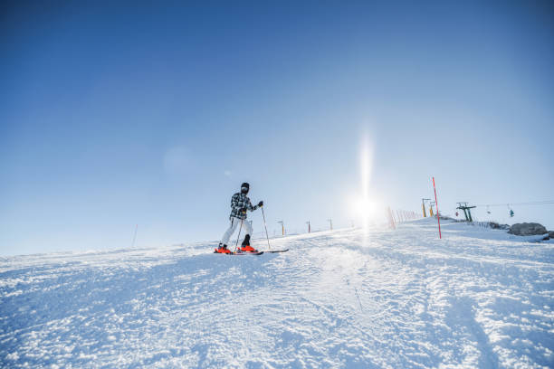 An Asian man enjoys skiing on a sunny winter day in the European Alps. The skier glides down a snowy slope, surrounded by clear blue skies, capturing the excitement of winter sports and the beauty of mountain landscapes.